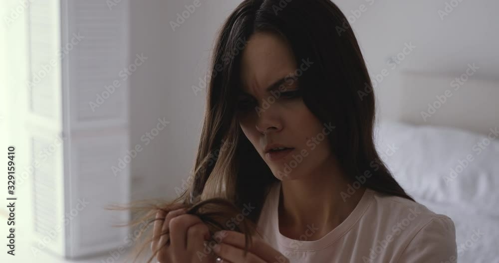 Worried young woman holding brittle fragile hair looking damaged and dry. Unhappy annoyed girl feeling upset about unhealthy split ends having hormone problems or vitamins deficiency concept. Worried young woman holding brittle fragile hair looking damaged and dry. Unhappy annoyed girl feeling upset about unhealthy split ends having hormone problems or vitamins deficiency concept.