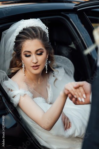Portrait of beautiful woman. Bride jewelry head sits in a black car on your wedding day. Portrait of the bride.  White lace dress. Perfect Make up. Hairstyle, wedding jewelry. Beautiful Woman