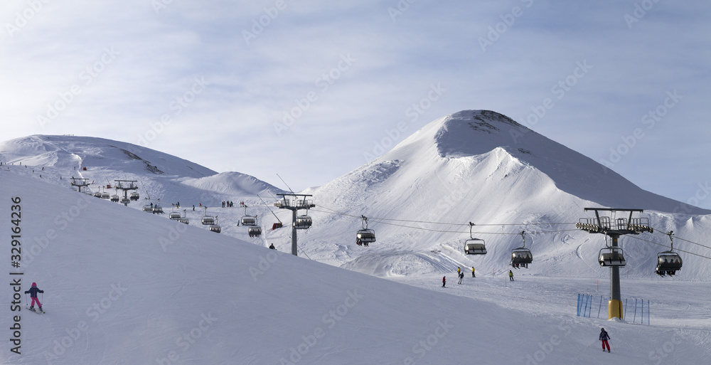 Panorama of snowy ski track prepared by snowcat, chair lift, skiers and snowboarders in ski resort