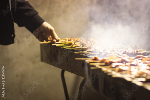 Chicken chunks skewers, grill, barbecue. On a metal bbq. In the grilling stages, hands holding the skewer. Dark night background, kosher food. Lots of smoke photo