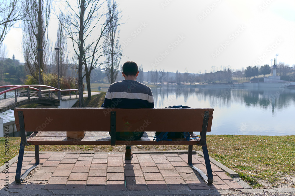 back view of a young man eating on an outdoor park bench on a sunny spring day back view of a young man eating on an outdoor park bench on a sunny spring day