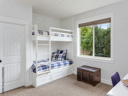 Children's bedroom in new luxury home with bunk beds and colorful comforters. Large window provides ample natural light