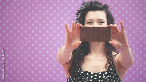 Pretty young lady with curly black hair and headband in polka-dots, showing a bar of chocolate to the camera. Blurred forefront. photo