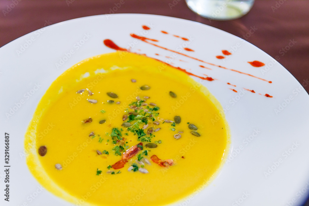 Yellow soup on white plate with spice in cafe. Close up shot of beautiful vegeterian food. Organic and health food with herd and vegetables. Interior of restraurant with food in bowl. Cream soup. Yellow soup on white plate with spice in cafe. Close up shot of beautiful vegeterian food. Organic and health food with herd and vegetables. Interior of restraurant with food in bowl. Cream soup.