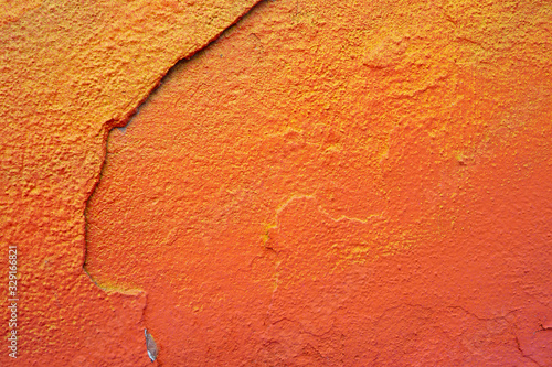 Large crack on an orange old plastered wall. Grungy background with cracks, chips and other irregularities for a design on a building theme.