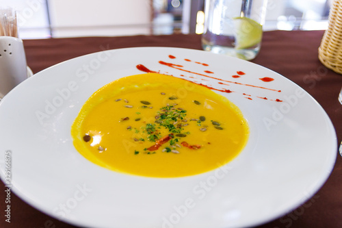 Yellow soup on white plate with spice in cafe. Close up shot of beautiful vegeterian food. Organic and health food with herd and vegetables. Interior of restraurant with food in bowl. Cream soup. photo