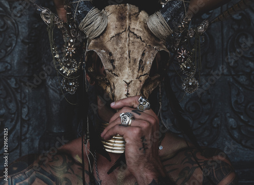 Fototapeta Tattooed masked skull ethnic pagan shaman sit on stage an ancient temple