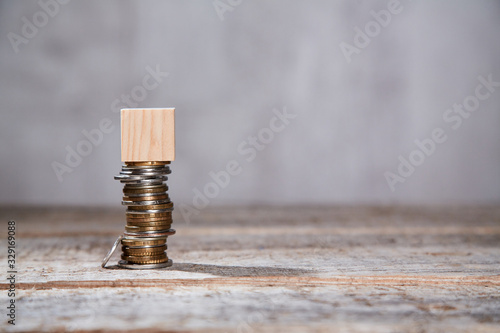 Pile of coins with wooden cube on top. Saving money for buying property. Mockup. Blurred background with copy space