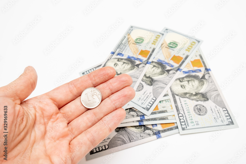 A hand holding one ruble coin and american dollar banknotes on background, ruble devaluation and usd-rub exchange rate concept