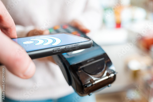 The seller holds a payment terminal, and the man pays for the purchase using a smartphone, online. Side view and close up. On the phone screen-wi-fi network. NFC concept and banking operations
