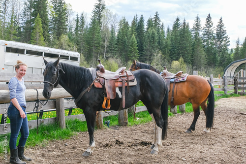 A young woman with to horses getting ready to go horse riding in Banff national park