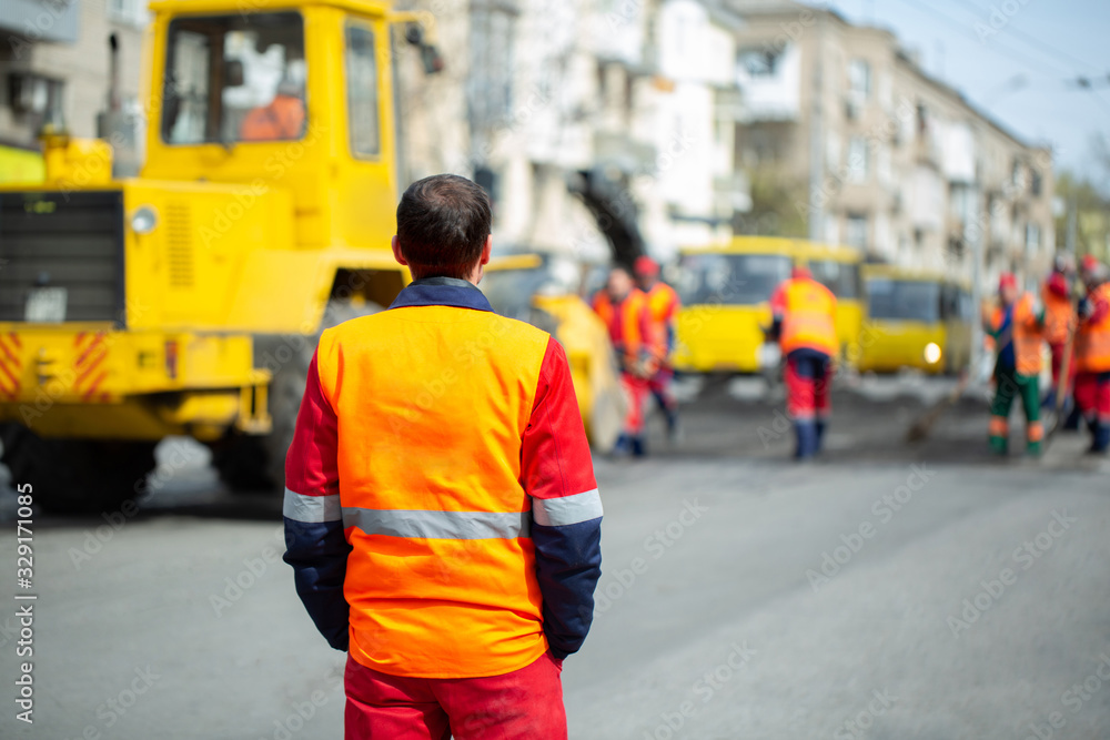 An employee in an orange uniform controls the process of road repairs. An employee in an orange uniform controls the process of road repairs.