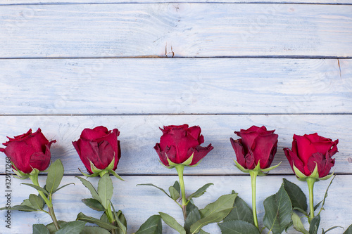 five red roses in a row on a wooden background