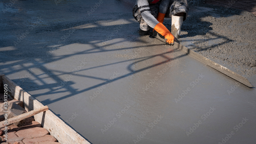 Cropped image of Asian construction worker using long triangle trowel to plastering cement on the floor in construction site