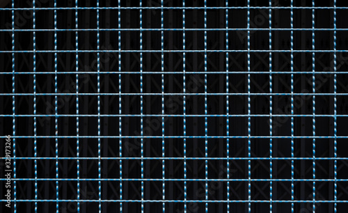 Close up grid pattern of the old blue steel mesh fence with blurred shutter door in dark background