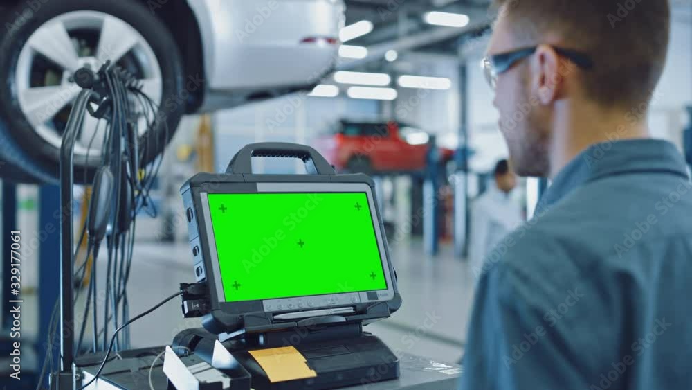 Car Service Mechanic is Running a Diagnostics Software on an Advanced Computer with Green Screen. Specialist Inspecting the Vehicle in Order to Find Broken Components and Errors in Data Logs. Car Service Mechanic is Running a Diagnostics Software on an Advanced Computer with Green Screen. Specialist Inspecting the Vehicle in Order to Find Broken Components and Errors in Data Logs.