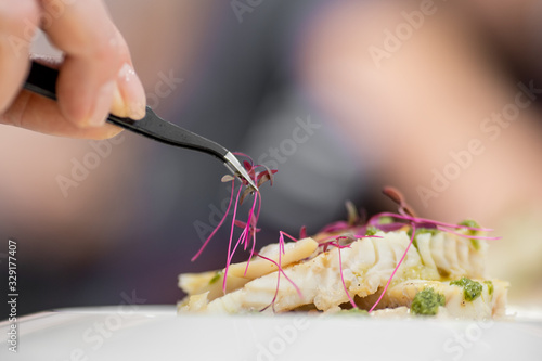 Chef with tweezers decorates with microgreens sprouts fish dish. Concept high art cooking, food decoration