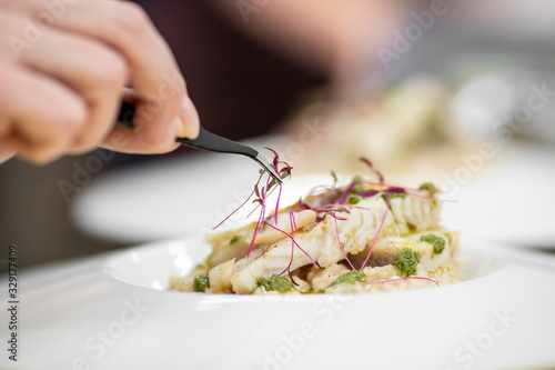 Chef with tweezers decorates with microgreens sprouts fish dish. Concept high art cooking, food decoration