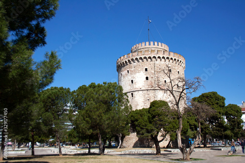 White tower of Thessaloniki surrounded by trees under clear blue sky on a sunny day
