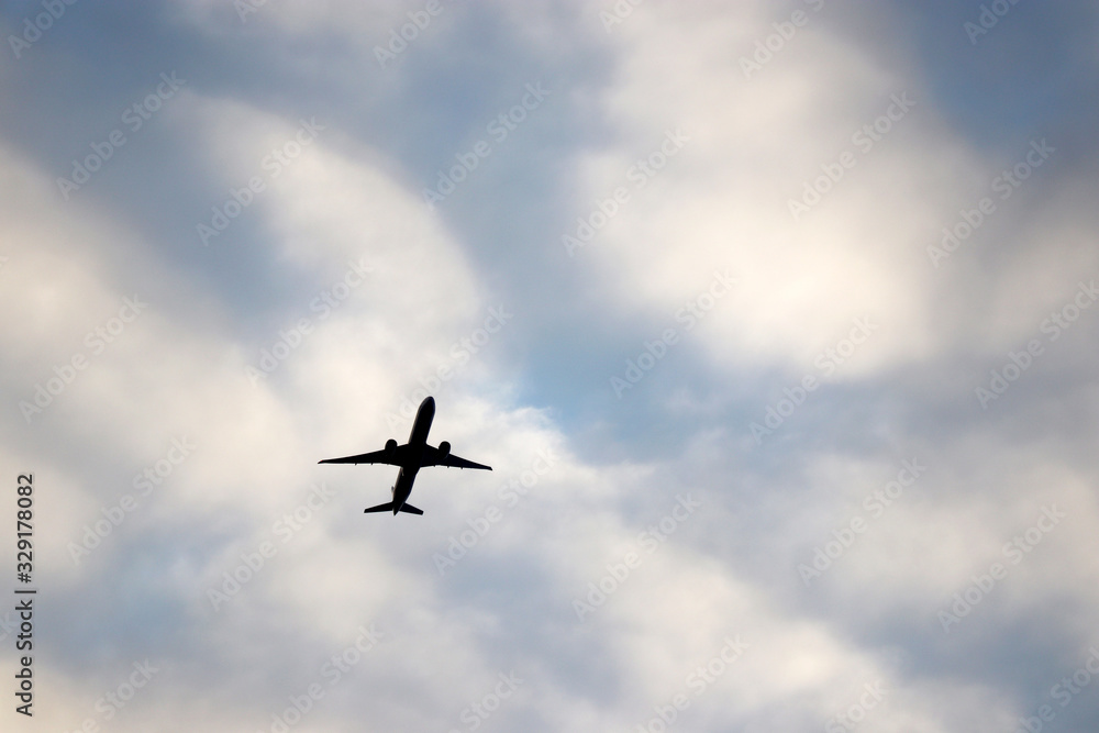 Airplane flying in the blue sky on background of white clouds. Silhouette of a commercial plane during the climb, travel and turbulence concept