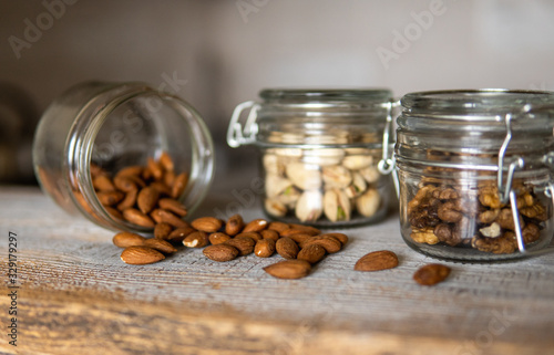 Almonds scattered on the white vintage table from a jar and with other nuts on background. Almond is a healthy vegetarian protein nutritious food. Almonds on rustic old wood.