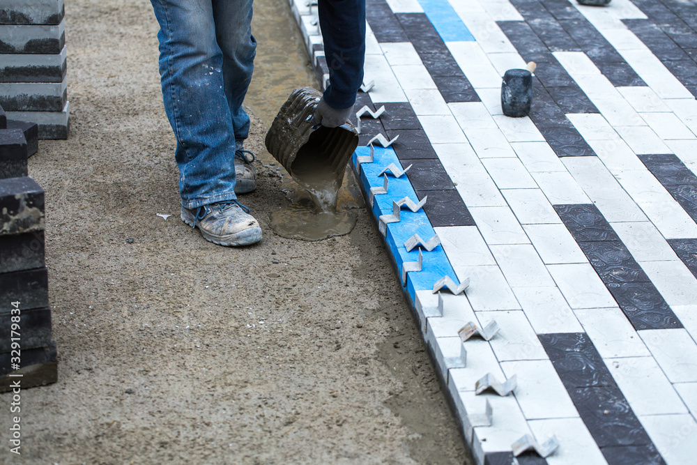 Construction work on pavement. Installation of concrete paver blocks on the sidewalk. Worker pours concrete mortar onto pre-prepared surface. Worker pours concrete mortar onto pre-prepared surface. Construction work on pavement. Installation of concrete paver blocks on the sidewalk. Worker pours concrete mortar onto pre-prepared surface. Worker pours concrete mortar onto pre-prepared surface.