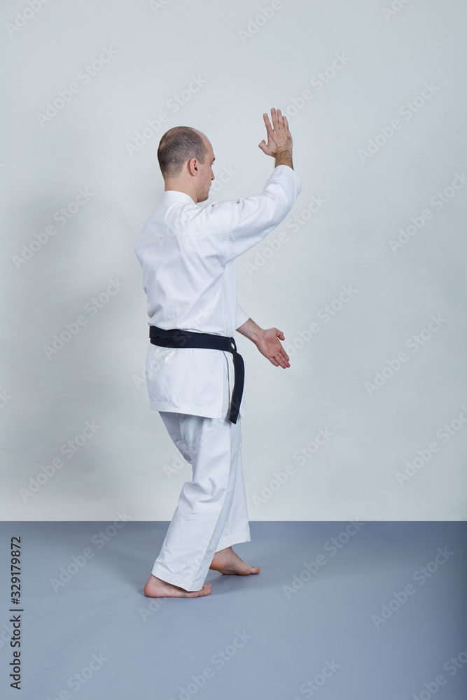 Young professional athlete performs formal karate exercises on gray cover Young professional athlete performs formal karate exercises on gray cover