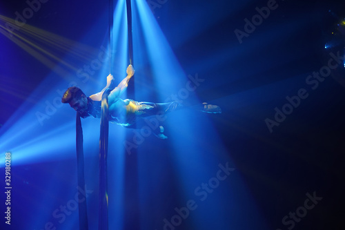 Fototapeta  Brazilian strong sexy man do performance on aerial silks in blue lights. Sport training gym and lifestyle concept. Black background