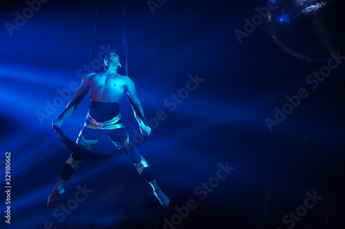 American strong sexy man do performance on aerial strap in blue lights.  Sport training gym and lifestyle concept. Black background.  © Dima