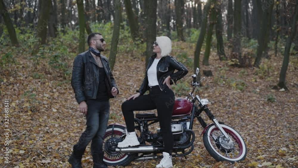 Happy biker comes to his woman and smiles in forest at motorcycle Happy biker comes to his woman and smiles in forest at motorcycle