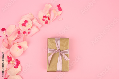 Flat lay composition with beautiful flowers and a gift box on a pink background. Space for text