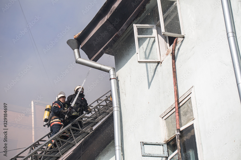 Firefighters on ladders in oxygen masks extinguish the fire in an old house in the middle of the city Firefighters on ladders in oxygen masks extinguish the fire in an old house in the middle of the city