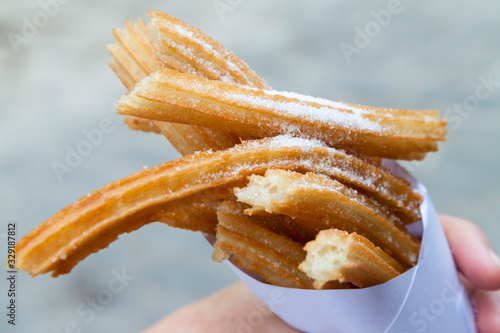 Foto Churros sprinkled with sugar held in a paper cone by a caucasian hand