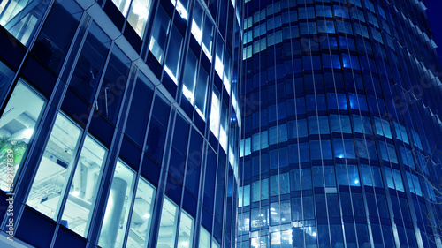 Night architecture - building with glass facade.Blue color of night lights. Modern building in business district. Concept of economics, financial. Photo of commercial office building exterior. Abstra