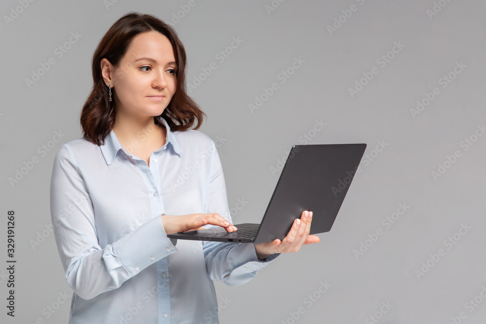 Charming young woman working freelance, remote from office, hold laptop, typing university essay, turn left smiling copy space, stand gray background joyful, browsing web using computer Charming young woman working freelance, remote from office, hold laptop, typing university essay, turn left smiling copy space, stand gray background joyful, browsing web using computer