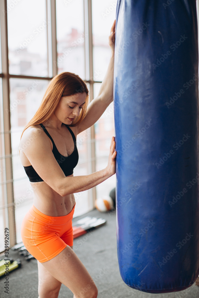Strong woman in sports clothes, trains with a boxing pear in a gym