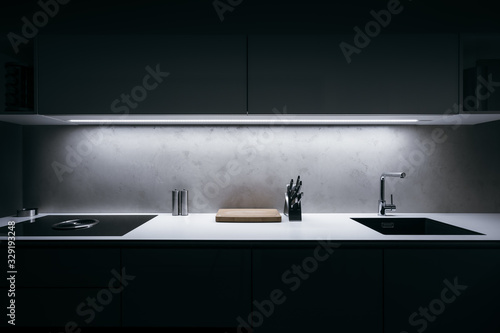 Modern kitchen in minimalist design during night with LED light strip and premium materials such as glass and concrete.Kitchen is complemented by basic kitchen utensils made of high quality materials.