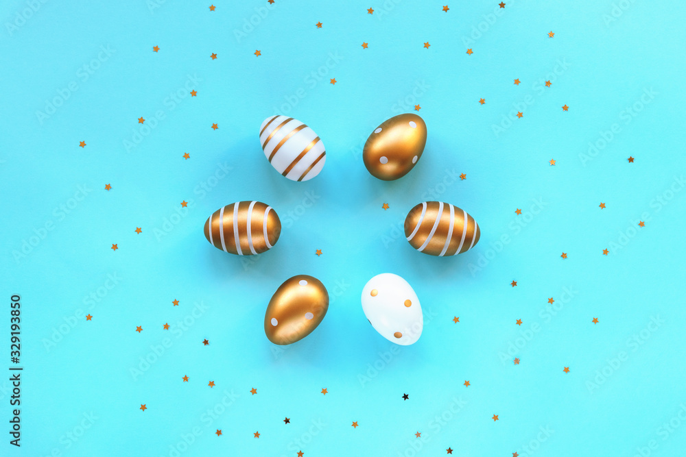 Painted gold and white eggs on a blue background with confetti. Easter concept. Top view, flat lay. Painted gold and white eggs on a blue background with confetti. Easter concept. Top view, flat lay.