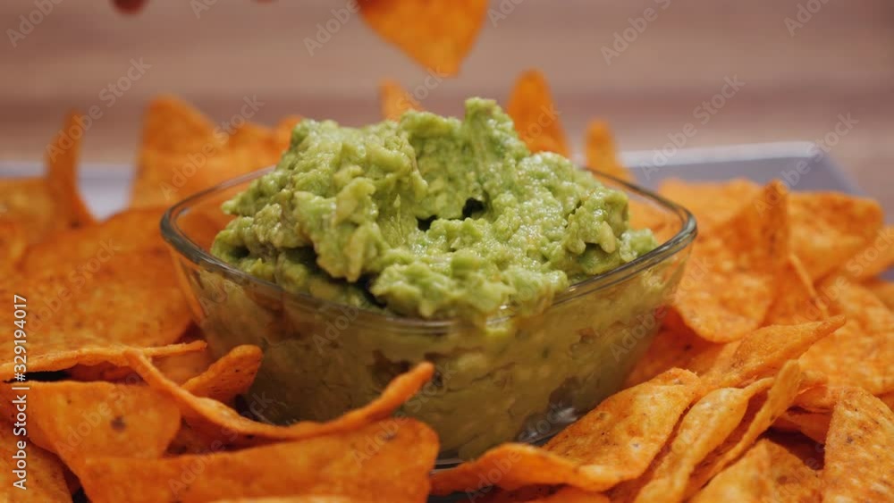 Hands taking delicious tortilla chips from a plate with guacamole in the center bowl - camera orbit around Hands taking delicious tortilla chips from a plate with guacamole in the center bowl - camera orbit around