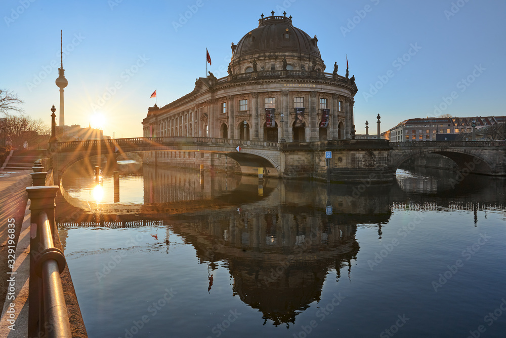 Berlin, Germany, Museum Island on Spree river and TV tower in the background at sunrise, Bode-Museum, cityscape early in the morning, reflections in the water, beautiful sun star