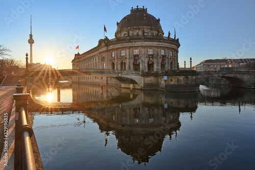 Berlin, Germany, Museum Island on Spree river and TV tower in the background at sunrise, Bode-Museum, cityscape early in the morning, reflections in the water, beautiful sun star