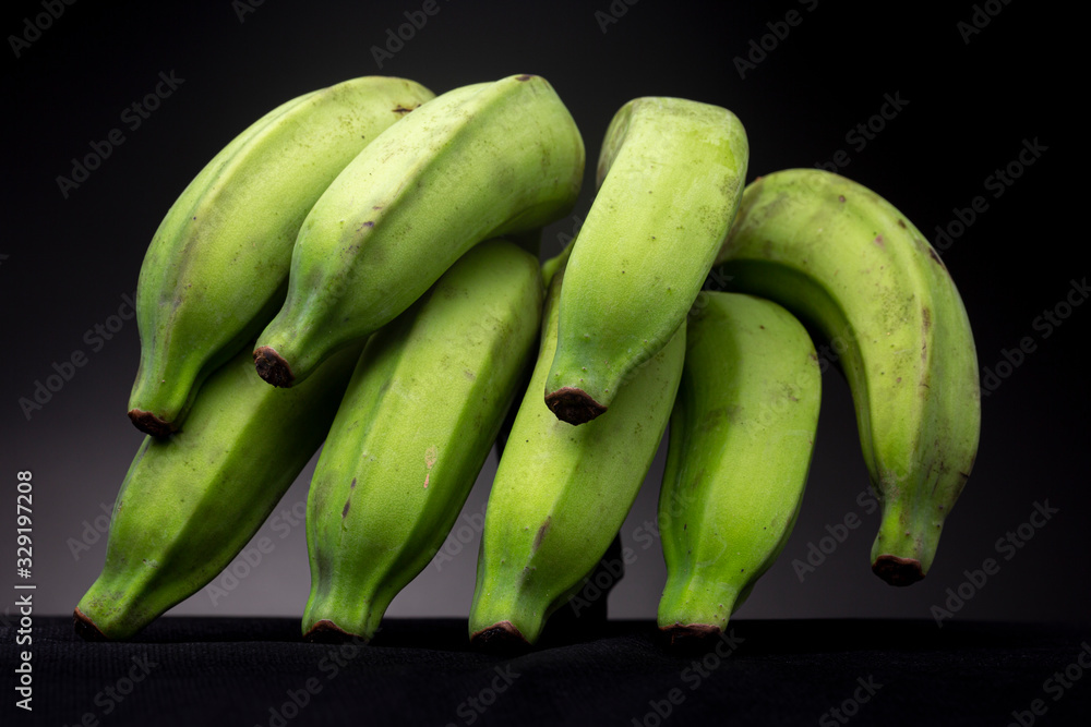 Brightly lit vibrant green banana on a black surface with dark grey studio background looking like a walking spider