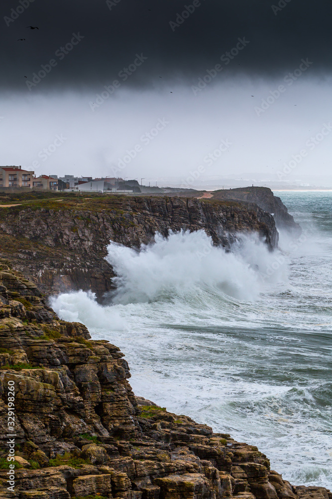A huge ocean waves breaking on the coastal cliffs in at the cloudy stormy day. Breathtaking romantic seascape of ocean coastline. Peniche, Portugal.