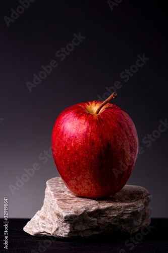 Moody shot of a vibrant bright red apple on a white textured rock against dark grey studio background. Still life of stone and fruit.