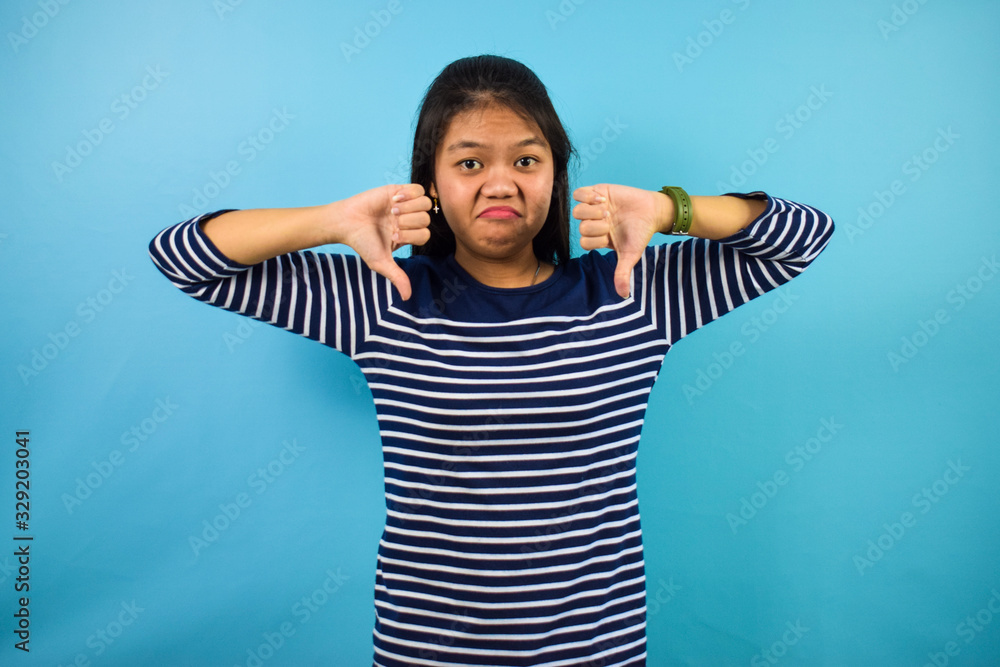 Portrait of Young beautiful asian women with blue isolated background, showing the thumbs down Portrait of Young beautiful asian women with blue isolated background, showing the thumbs down