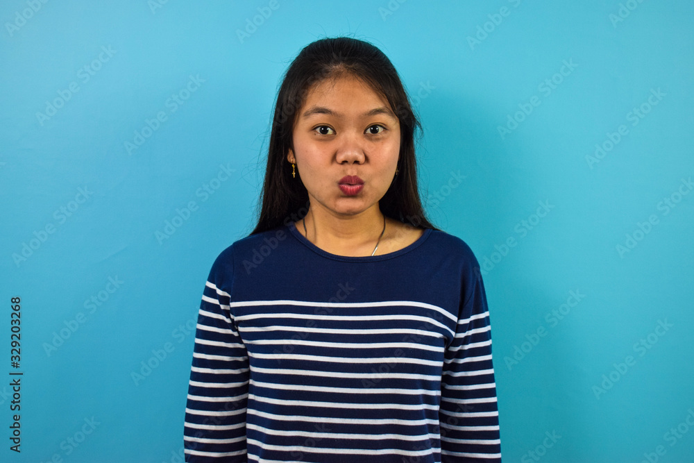 Fototapeta premium Portrait of Young beautiful asian women with blue isolated background, lips folded for kiss