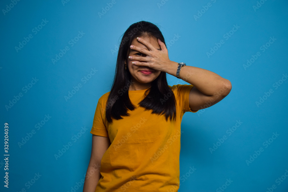 Portrait of Young beautiful asian women with blue isolated background, looking through fingers with embarrassed expression Portrait of Young beautiful asian women with blue isolated background, looking through fingers with embarrassed expression