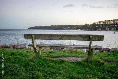 Wooden bench close by the sea in harbour. There is a person on SUP paddle board in background.