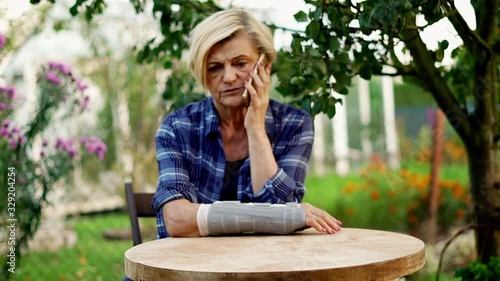 Senior woman sitting with her arm in a sling and talking on cellphone in the garden photo