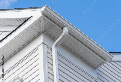Colonial white fiber cement horizontal vinyl lap siding, soffit with ventilation,  gutter and guard, eaves with elbow, drip, on a new construction American single family home photo